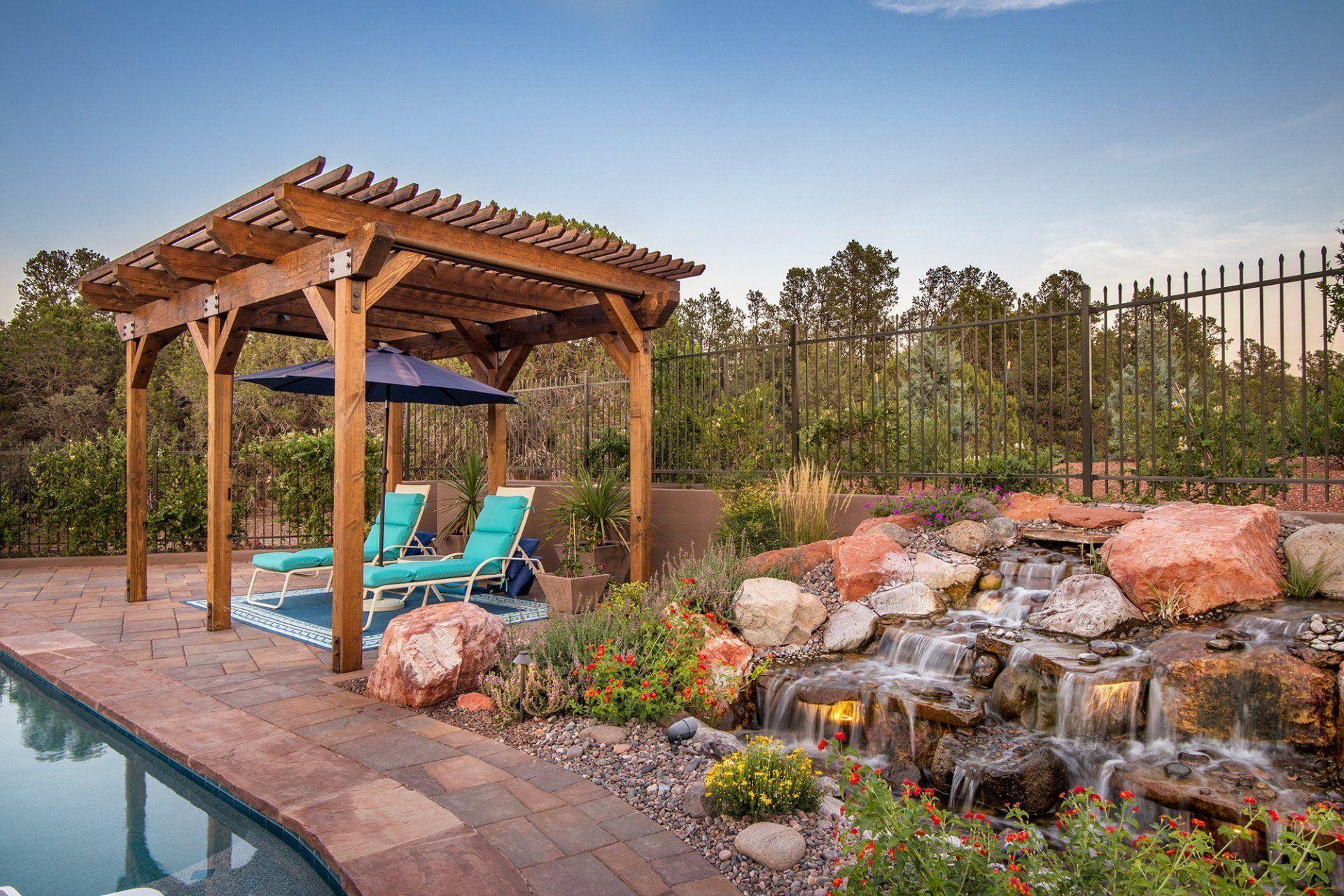 There is a waterfall in the backyard with a pergola and chairs.