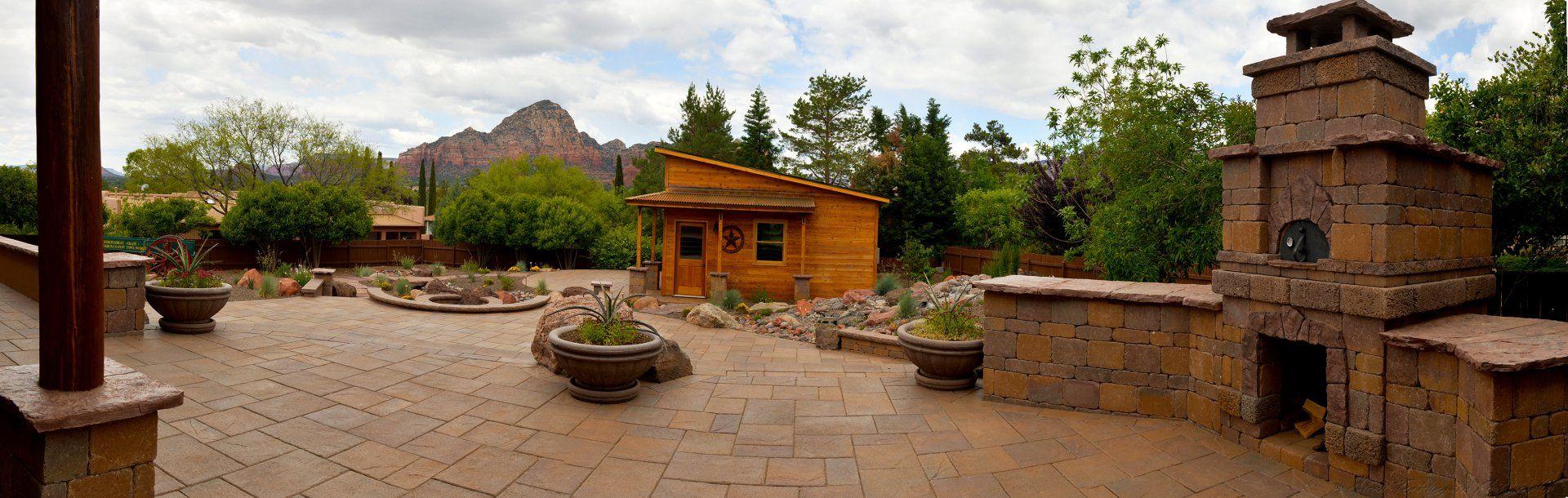 Panoramic paver patio with an outdoor fireplace, planters and a wooden shed