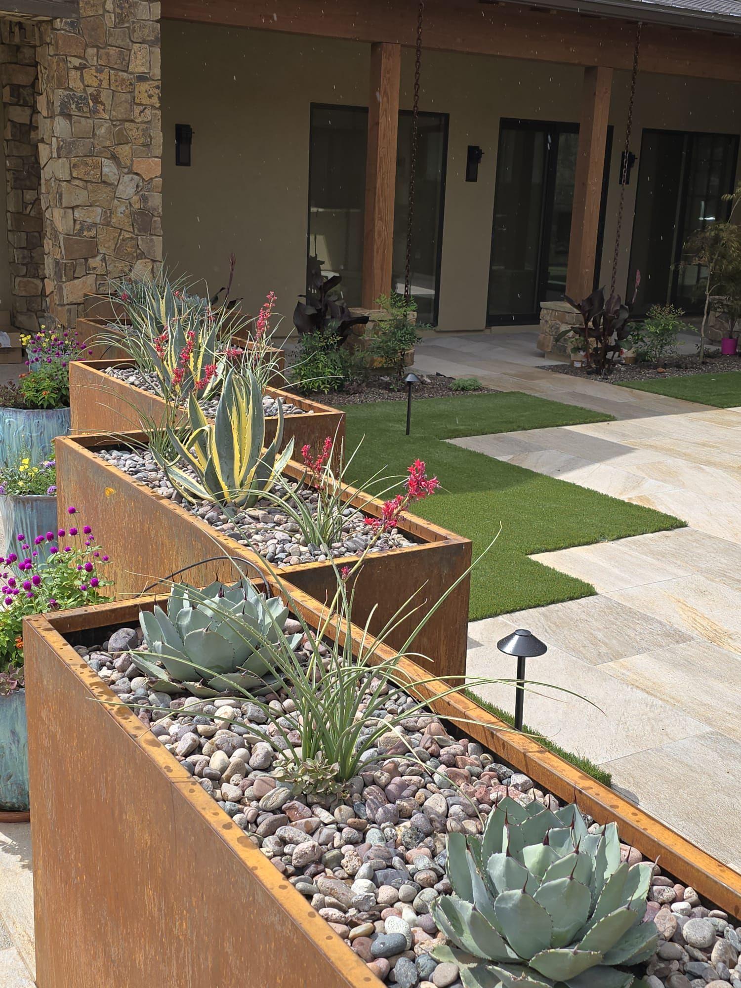 Corten steel planters with agave, succulents and river rock beside a courtyard lawn