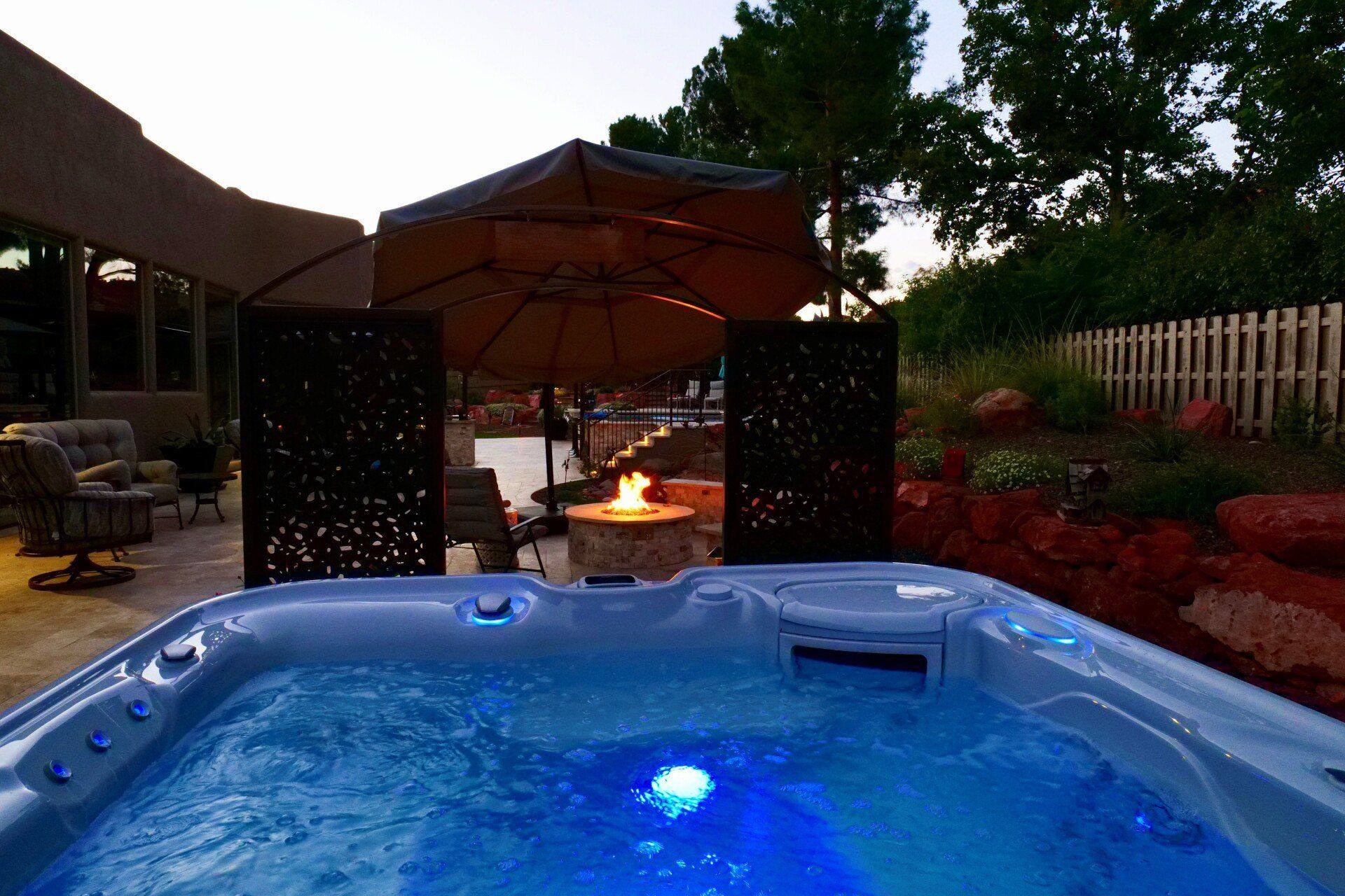Hot tub lit blue at dusk beside a patio fire pit