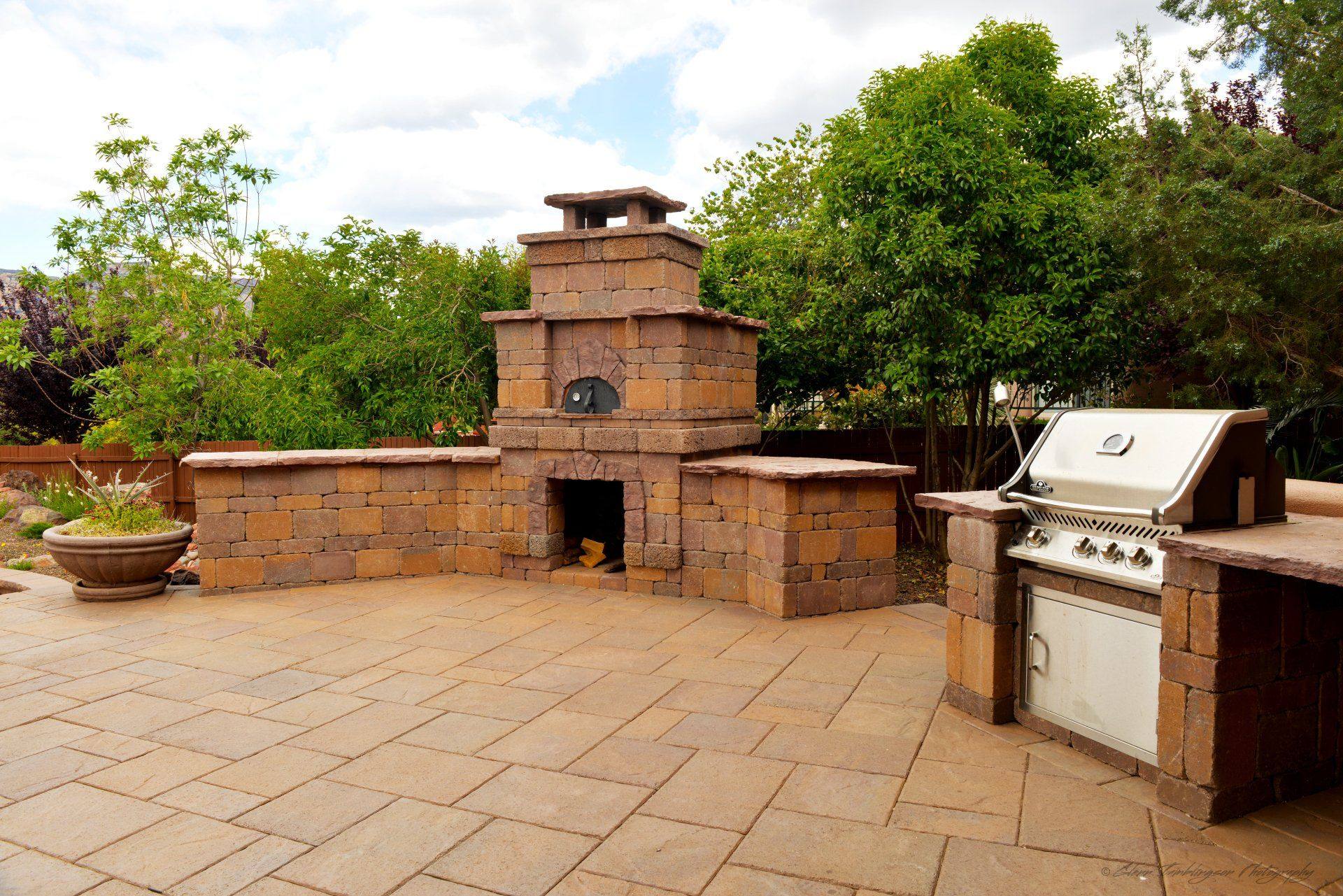 Outdoor kitchen with a stone pizza oven, fireplace and built-in grill on a paver patio