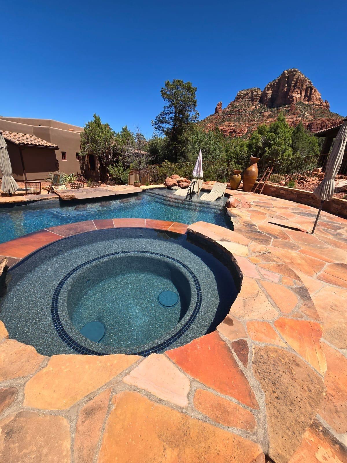 Round spa beside a pool on a flagstone deck with red rock formations beyond