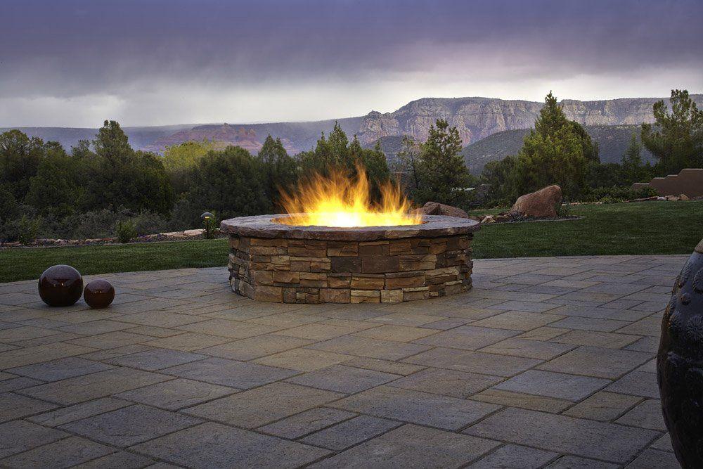 A fire pit is lit up on a patio with mountains in the background.