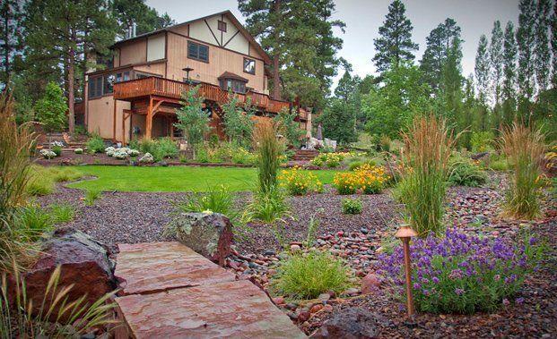 Two-story home with a wooden deck, overlooking a landscaped garden with a stone path and colorful plants.