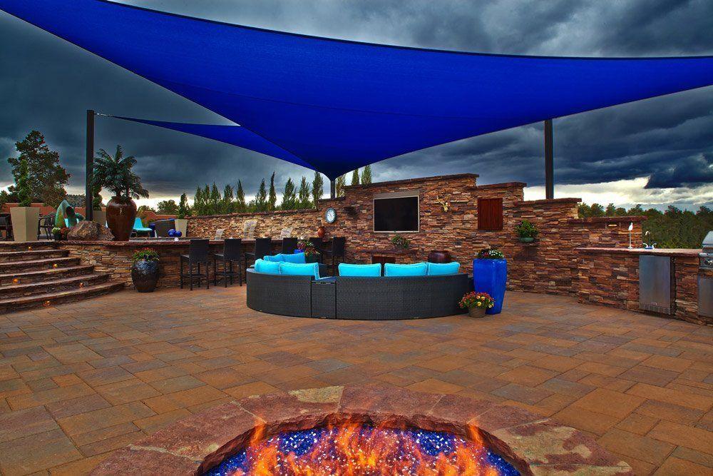 There is a fire pit in the middle of the patio under a blue umbrella.