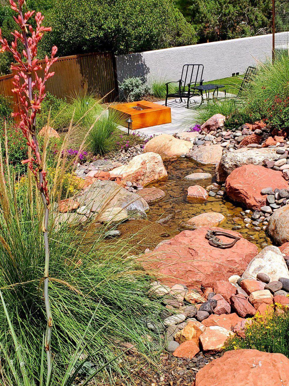 Rocky stream bed with red yucca leading to a patio with a fire pit and chairs